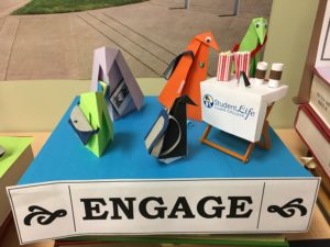 origami penguins visit a student life table with popcorn and coffee near a sign reading "Engage."