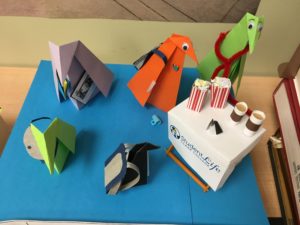 origami penguins with backpacks and messenger bags line up for coffee and popcorn