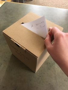 A hand places a piece of paper into the summer reading suggestion box.