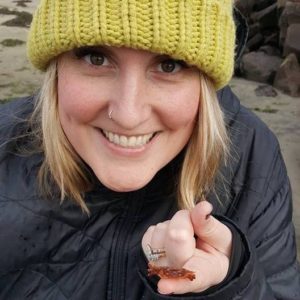 Smiling woman wearing warm coat and hat holding a small crab on her finger