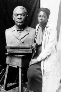 Photo of artist Selma Burke standing next to her work in 1935