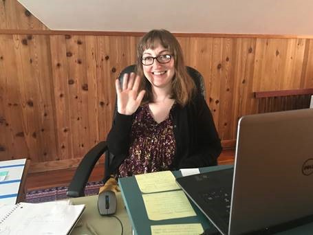 Julie Austad smiles at you from her home workstation. Sticky notes cover the surface of her laptop stand.