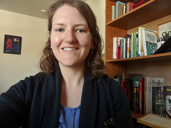 Laura Nagel smiles at you with a bookshelf in the background and artwork on the adjacent wall.