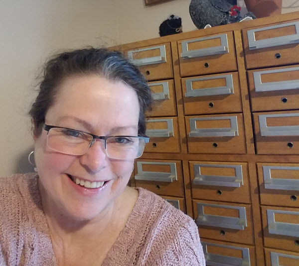 Tammy Boyer smiles at you in front of her light-toned, wood card catalog.
