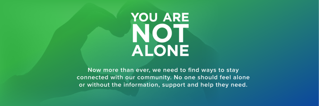 Image text reads: you are not alone. Now more than ever, we need to find ways to stay connected with our community. No one should feel alone or without the information, support and help they need. End text. The background of the image is someone holding their hands in the shape of a heart. The background is a blue to green gradient.