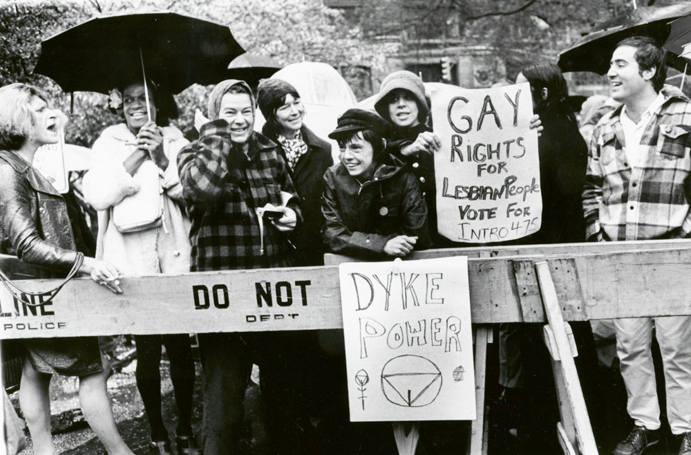 An image of queer people protesting. It includes several white people, as well as Marsha P. Johnson and Sylvia Rivera, two trans women of color.