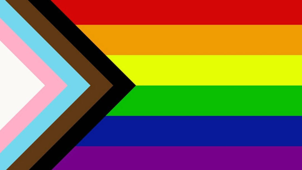 The Progress Pride Flag. On the left-hand side there are triangle stripes representing the trans community and queer people of color. The rest of the flag is the traditional rainbow stripes.