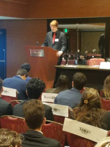 Clark Model UN delegate giving a speech in front of other student delegates representing various countries.