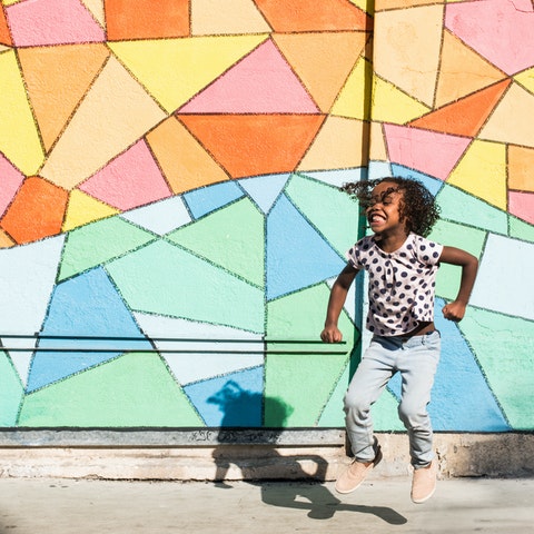 Black girl jumping in front of colorful wall