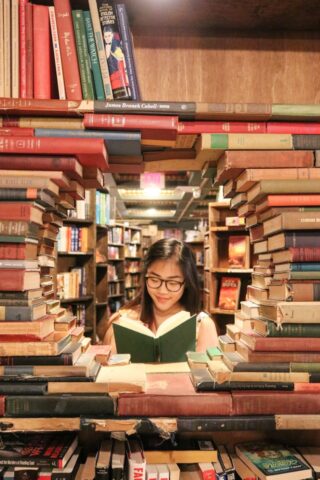 Woman reading a book framed by a circular stack of books. She is in a room filled with books.