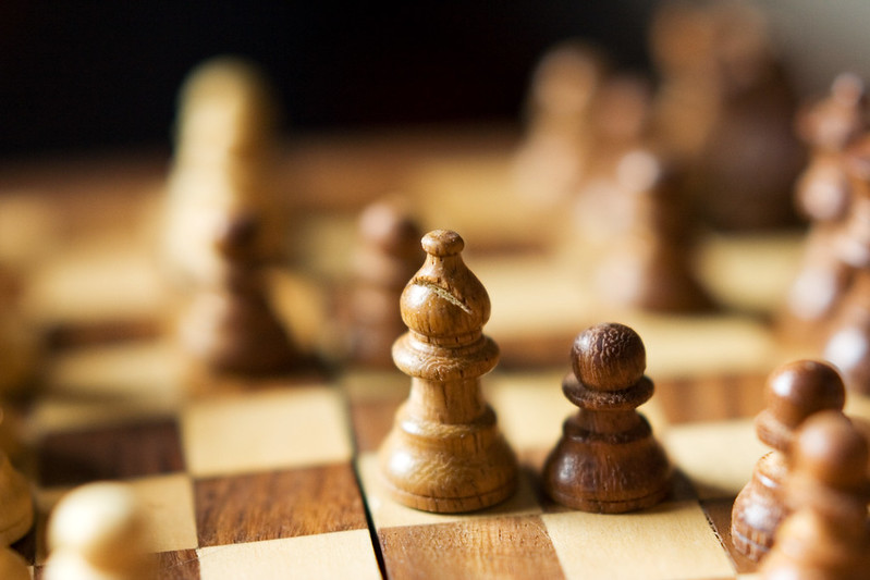 A bishop and pawn take a sharp center on the blurred background of a brown and white wooden chess board