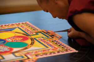 A monk leans over intricate designs of colored sand.
